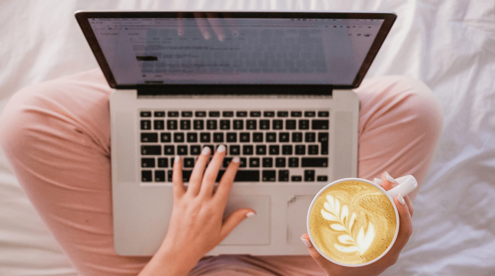 woman using her laptop while holding a coffee